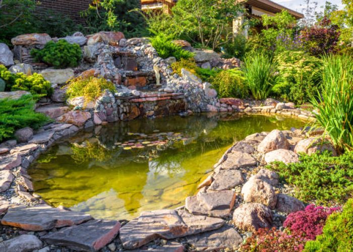 Landscape design of home garden close-up. Beautiful landscaping with small pond and waterfall. Landscaped place with rocks at country house. Stone landscaping in luxury backyard or yard in summer.